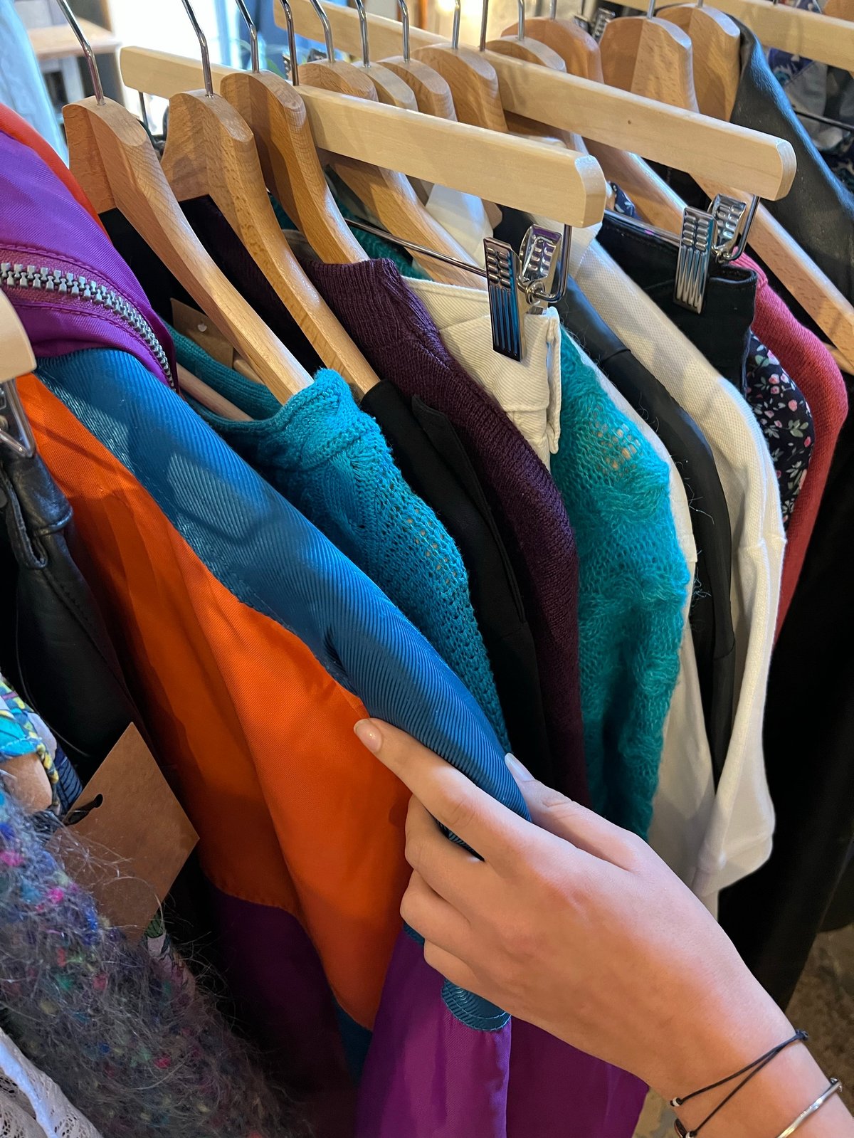 Customer's hand selecting quality-graded pre-owned garments on the rack at Empire Buddies