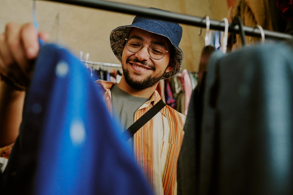 Smiling young man browsing curated secondhand clothing racks at Empire Buddies