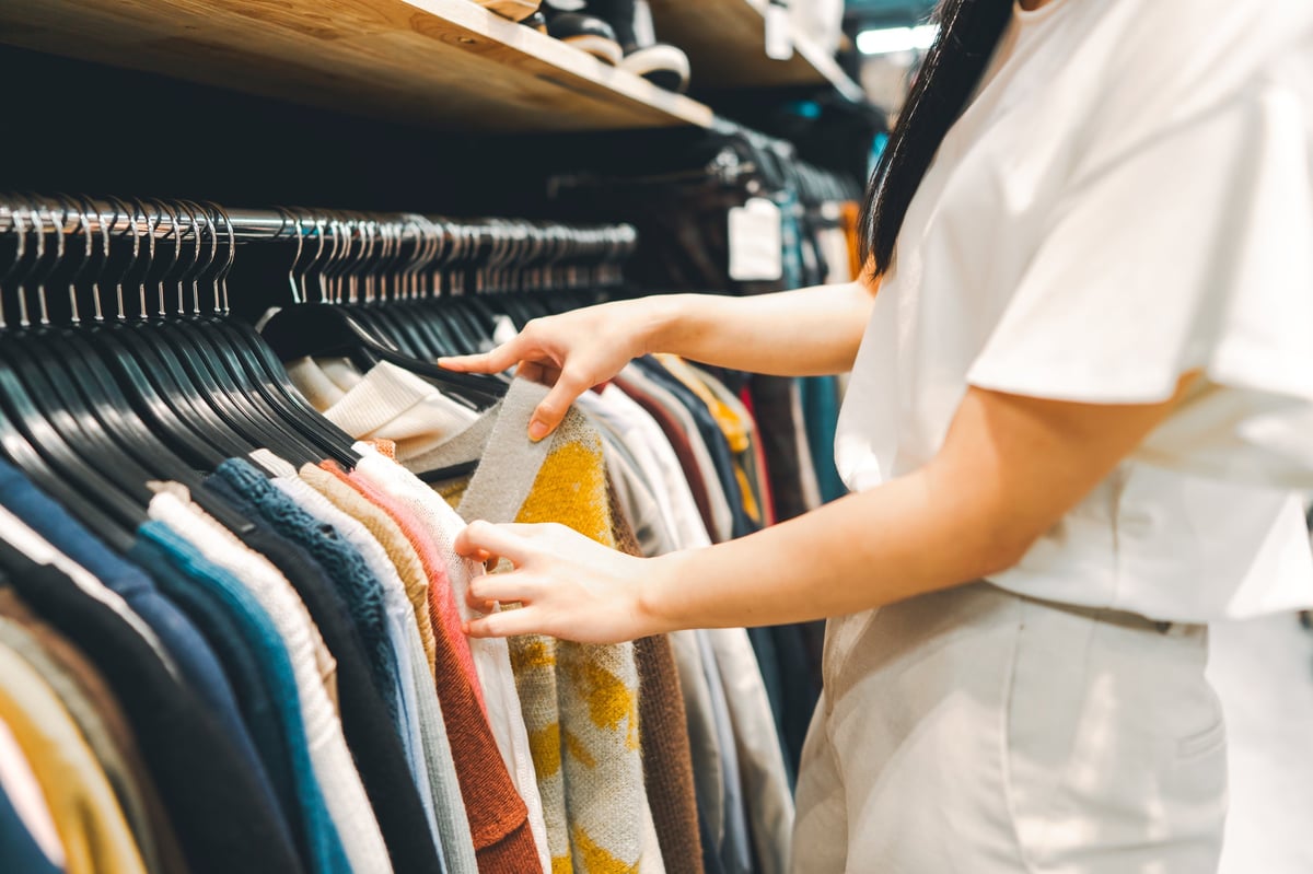 Black woman's hand browsing pre-owned clothing on hangers